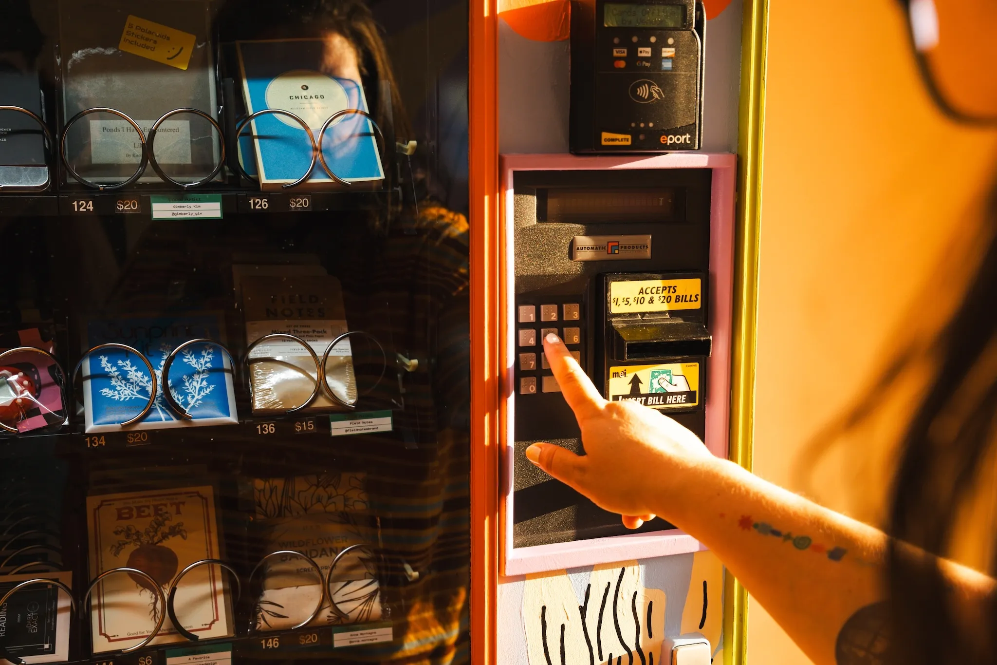 A hand presses buttons on a multicolored Good Things Vending machine.