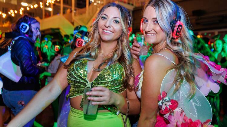 Two women in Halloween costumes dance while wearing headphones.