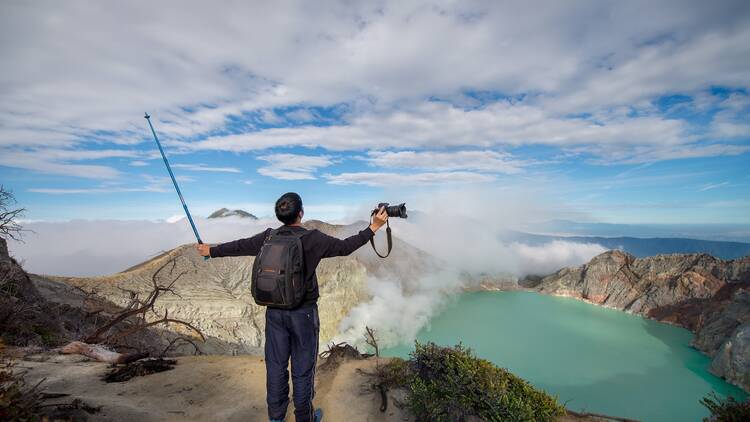 Asian man holding trekking pole and camera on Kawah Ijen volcano summit