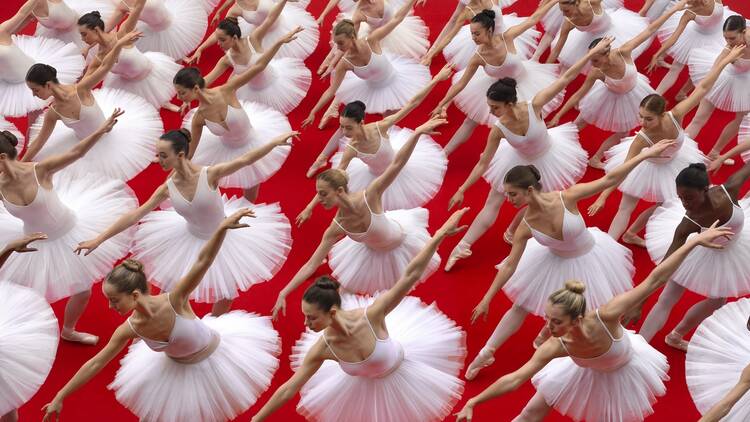 Rows of ballet dancers in white posing in front of a red background