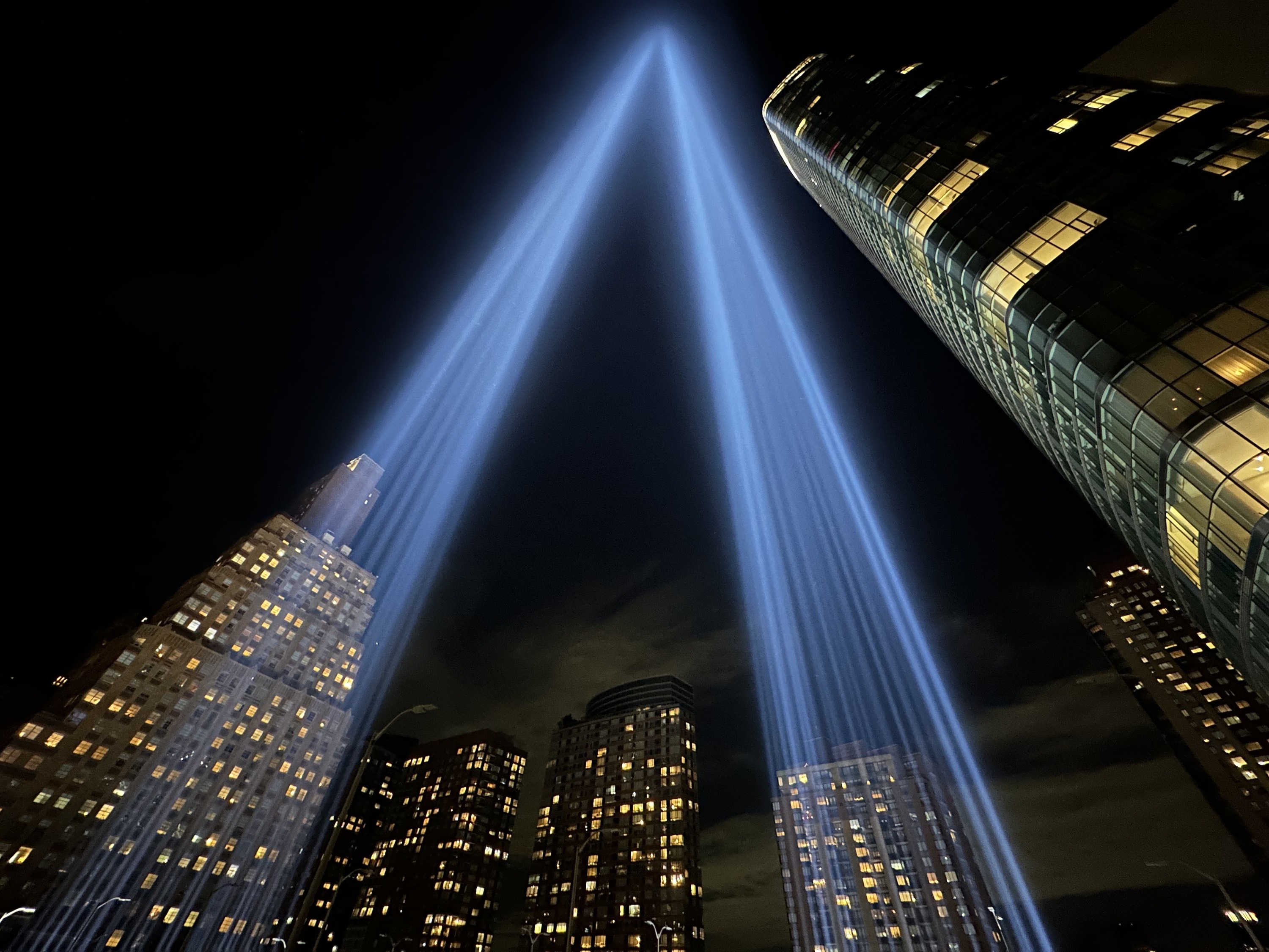 Beams of blue light are projected into the sky as part of Tribute in Light, a 9/11 art installation. Skyscrapers are see in the background.
