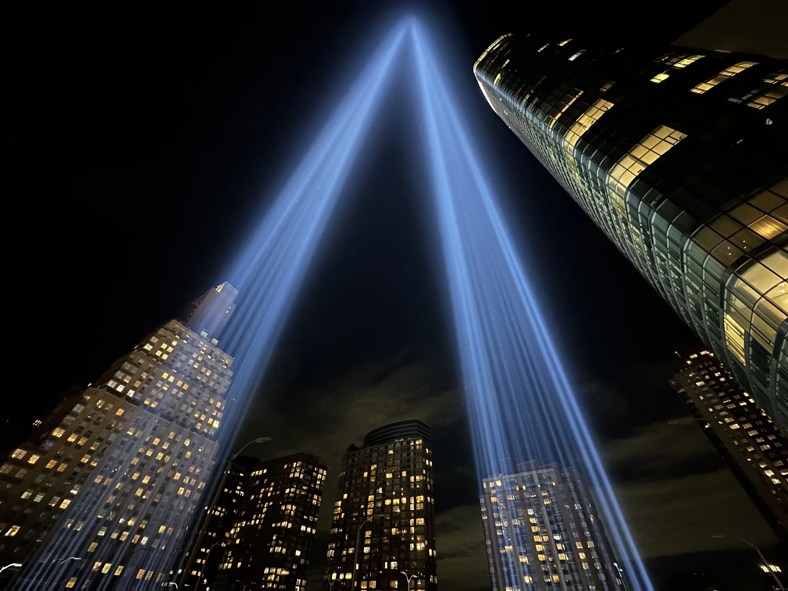 Beams of blue light are projected into the sky as part of Tribute in Light, a 9/11 art installation. Skyscrapers are see in the background.