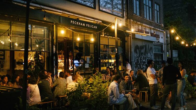 Crowds of people sitting at tables outside the Peckham Pelican as night falls