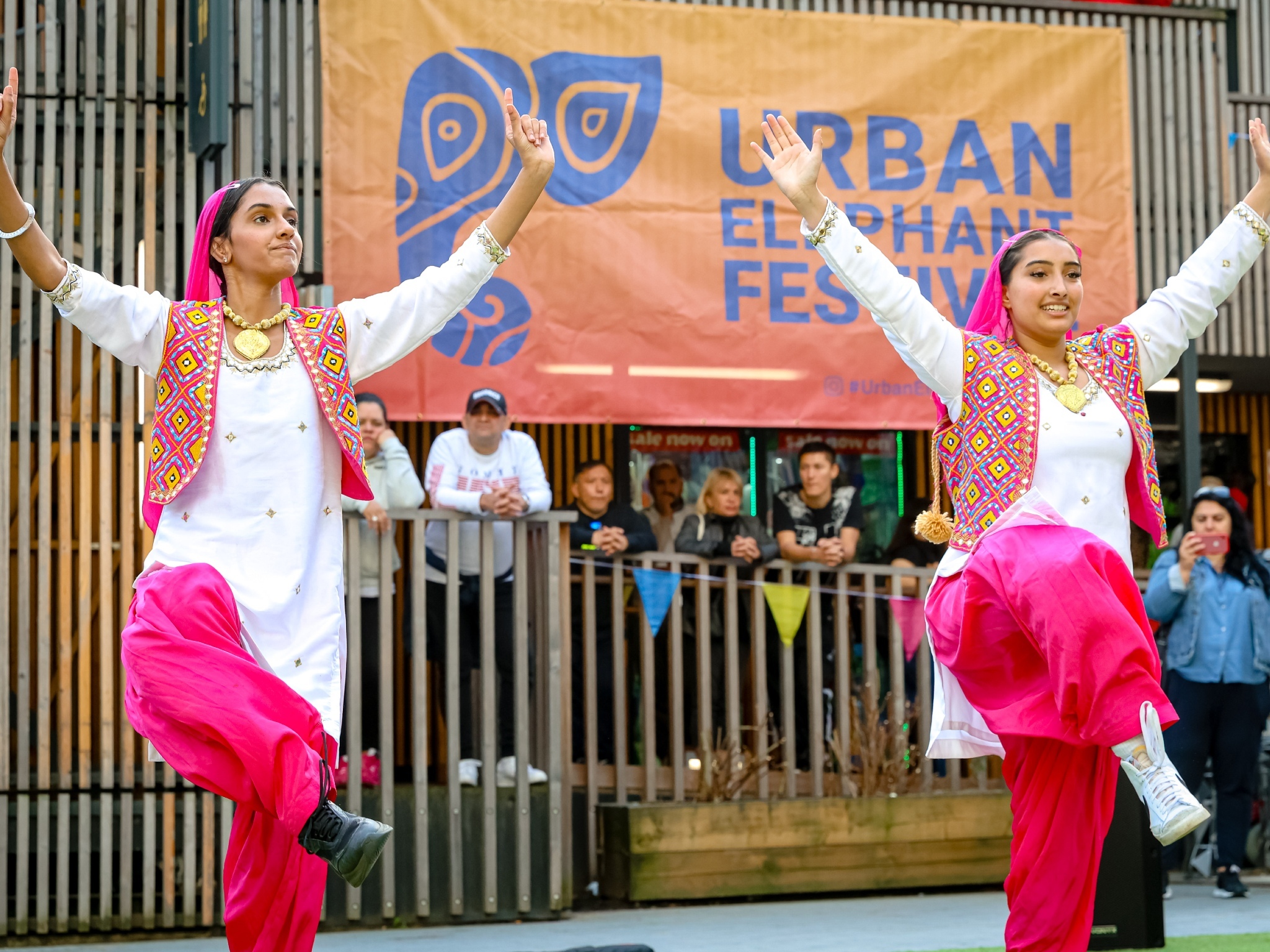 Two dancers wearing traditional Indian costume performing in front of a sign for Urban Elephant Festival