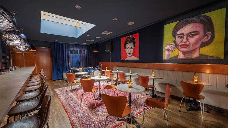 A blue room with marble tables and two large canvas drawings of women