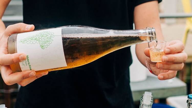 A person pouring a bottle of cider in a small cup