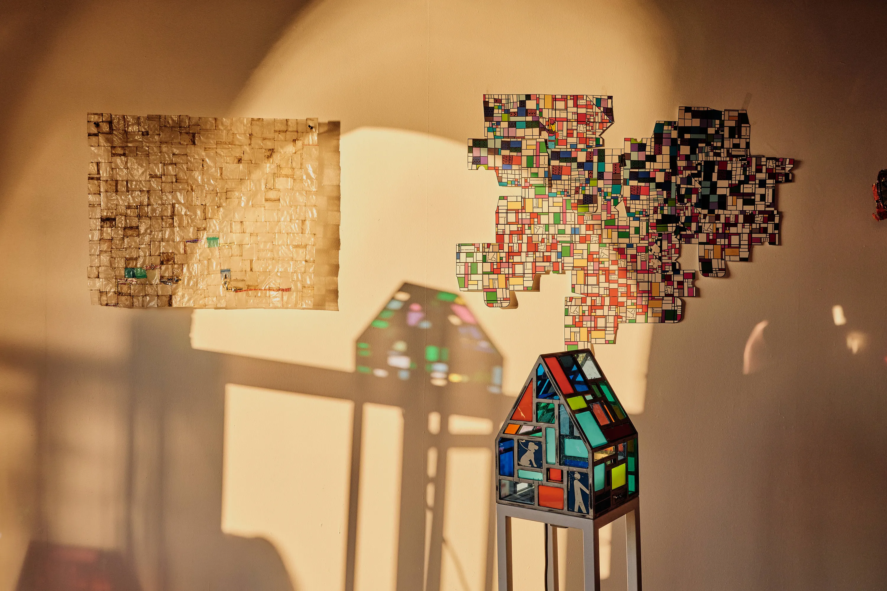 A tiny colorful house sculpture in front of two pieces of artwork on the wall.