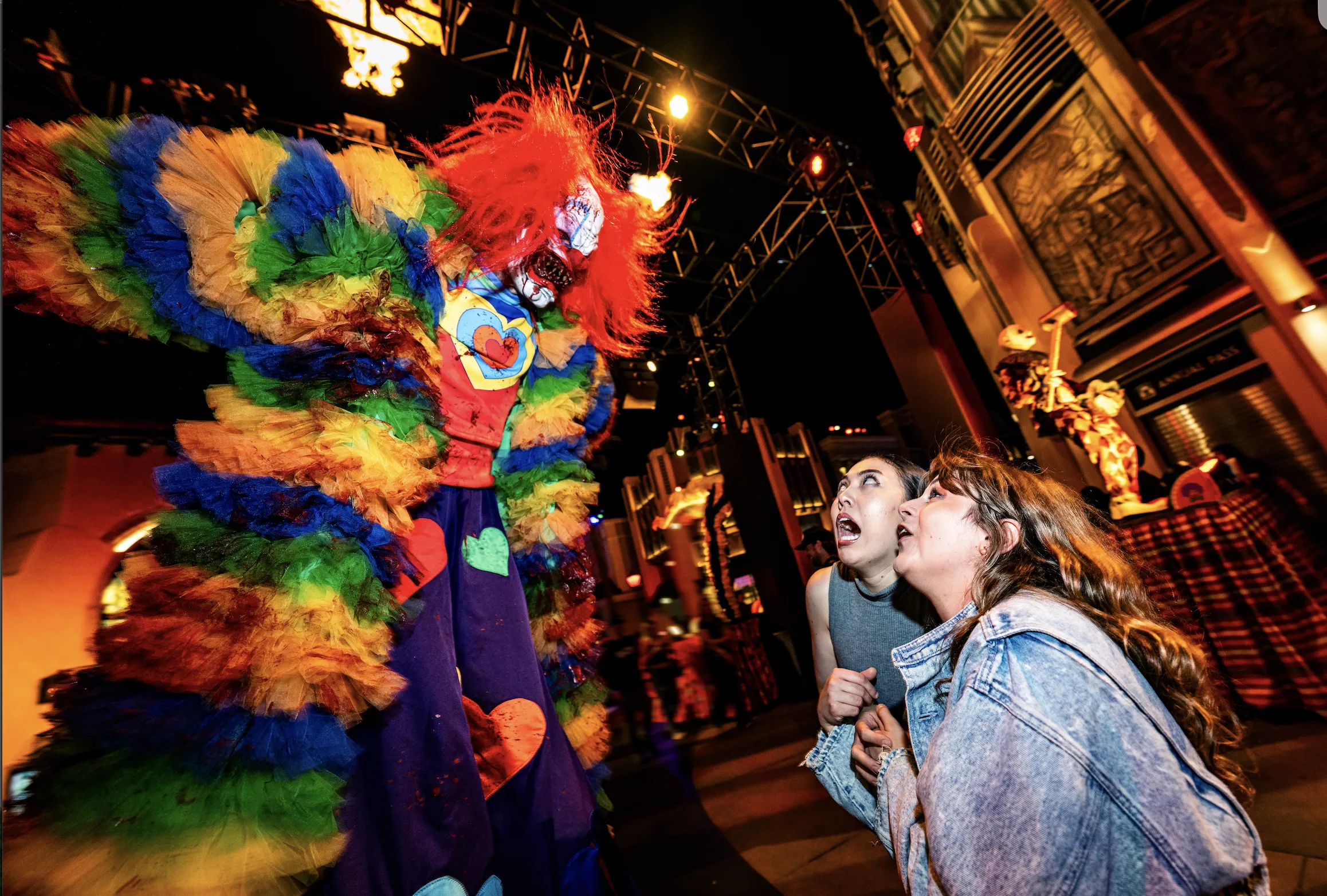 A clown on stilts towers over two scared girls.