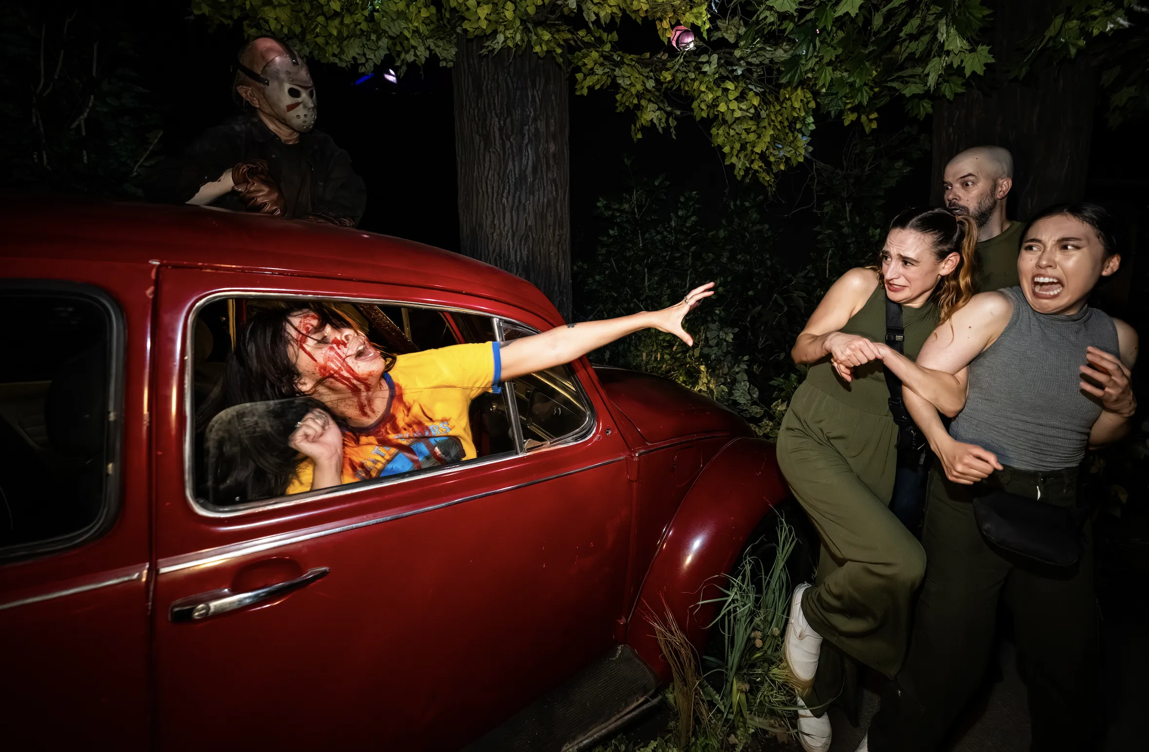A girl with blood on her face reaches out of a Volkswagen Beetle as Jason looms behind her.
