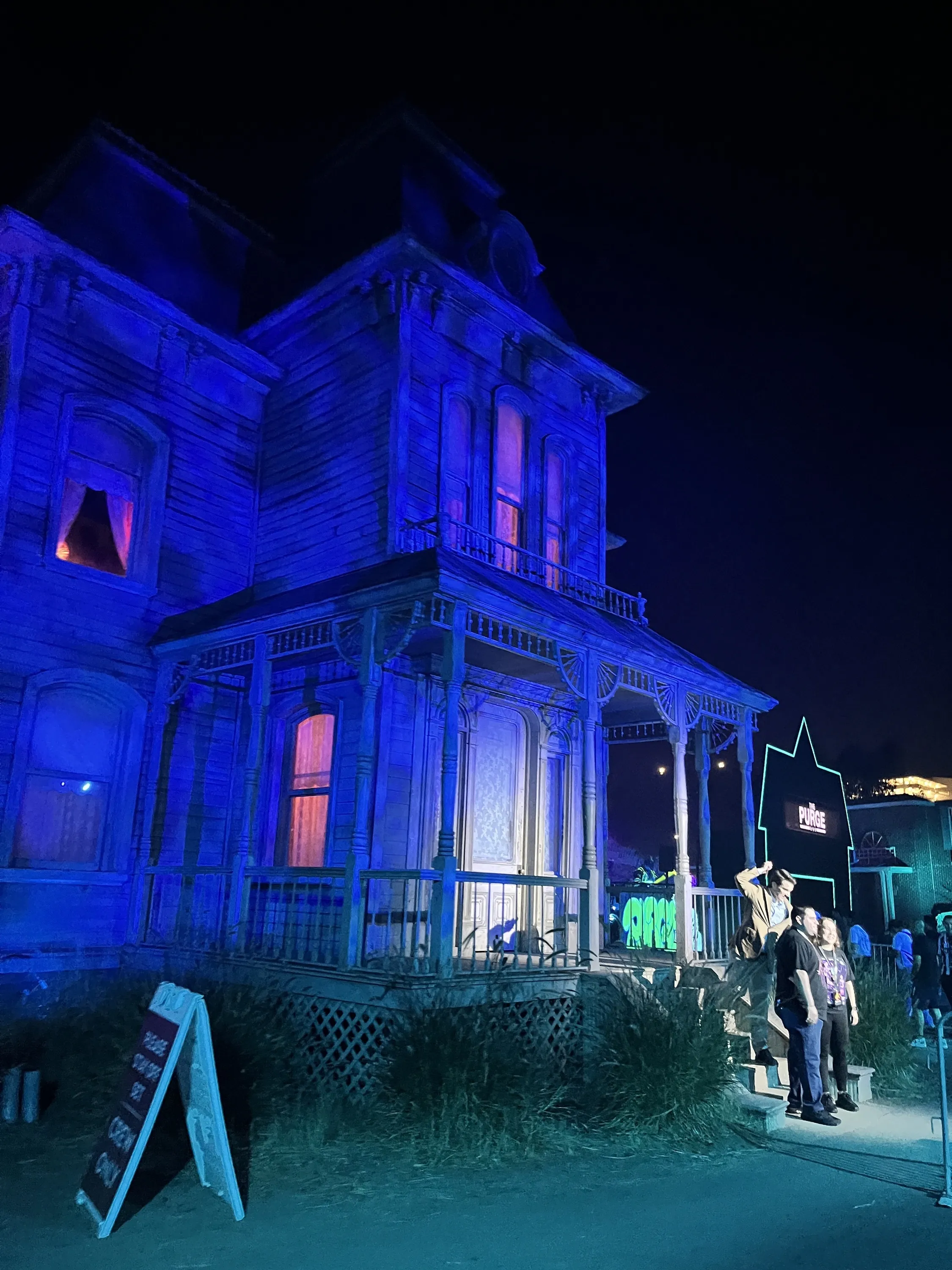 A man dressed up like Norman Bates poses with two guests in front of the Psycho House.