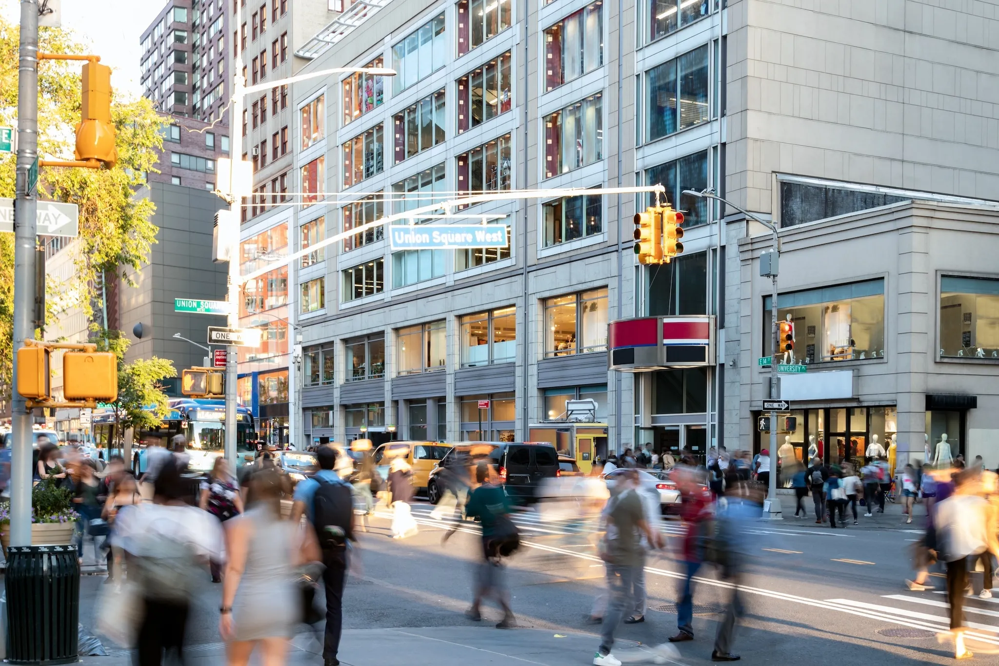 Crowds of people walking across the busy intersection on 14th Street at Union Square Park in New York City NYC past the cars and buildings