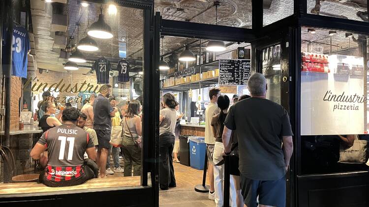 A line of people waiting outside the door of L'Industrie Pizza
