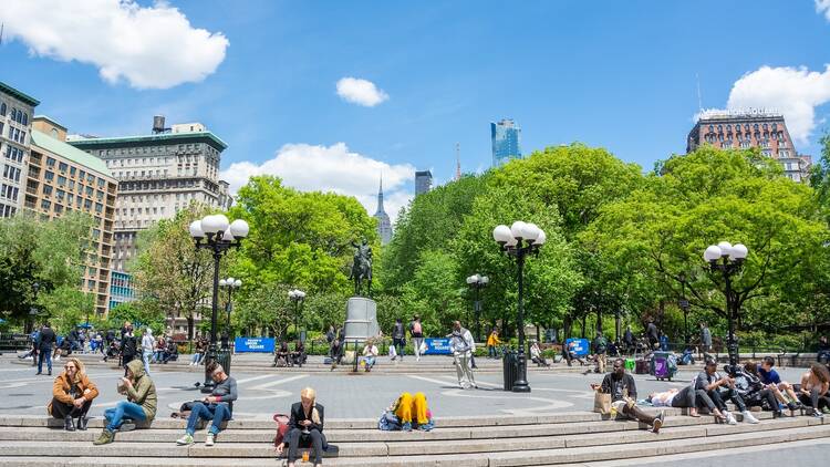 Union Square in New York City. View looking north, toward George Washington statue and Empire State Building, with people sitting on the stairs and buildings
