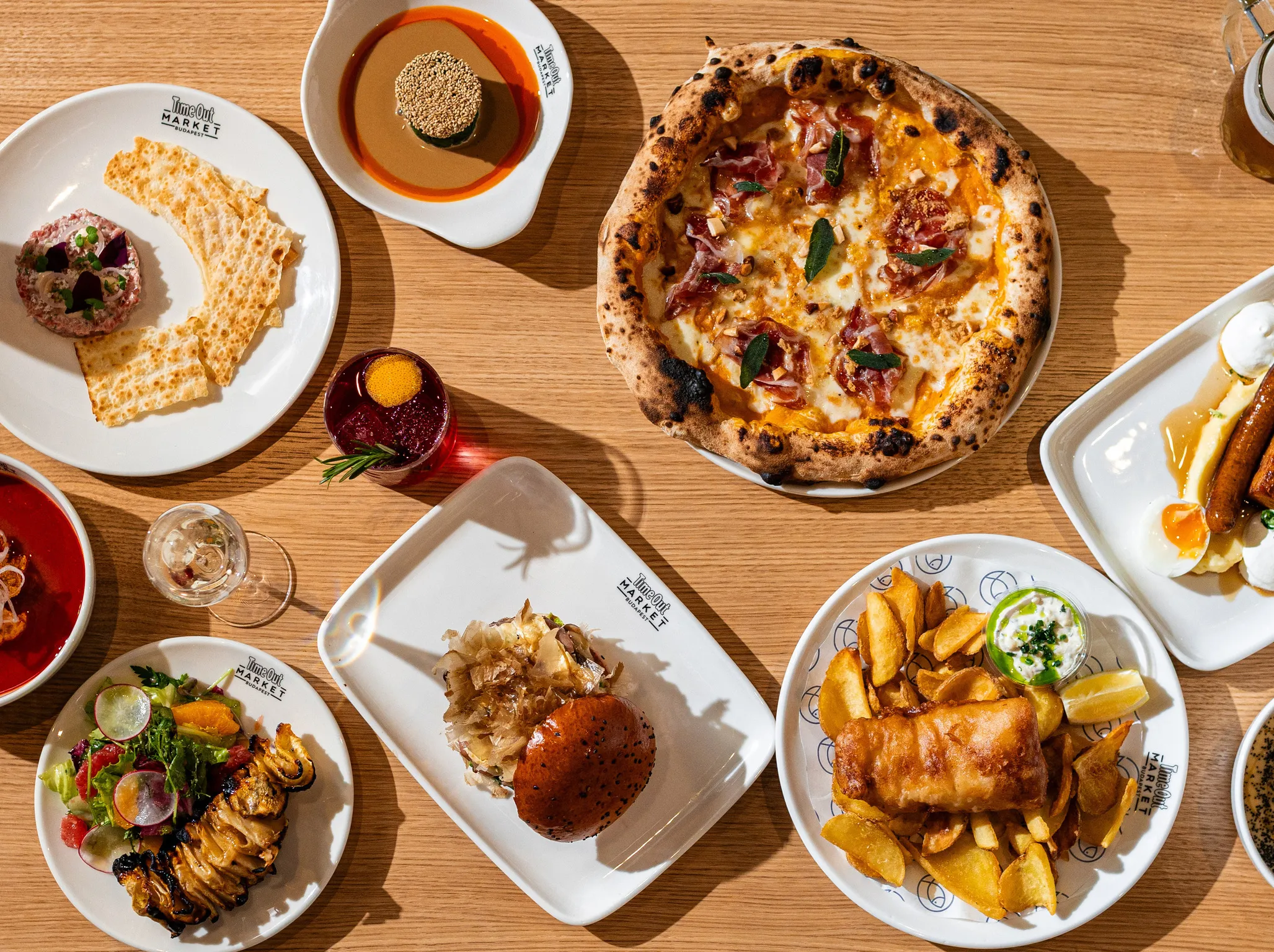 Hamburger, pizza, spenót, fish and chops, marhatatár, rakott burgonya, bor, koktél és sör a Time Out Market Budapest asztalán tányéron tálalva