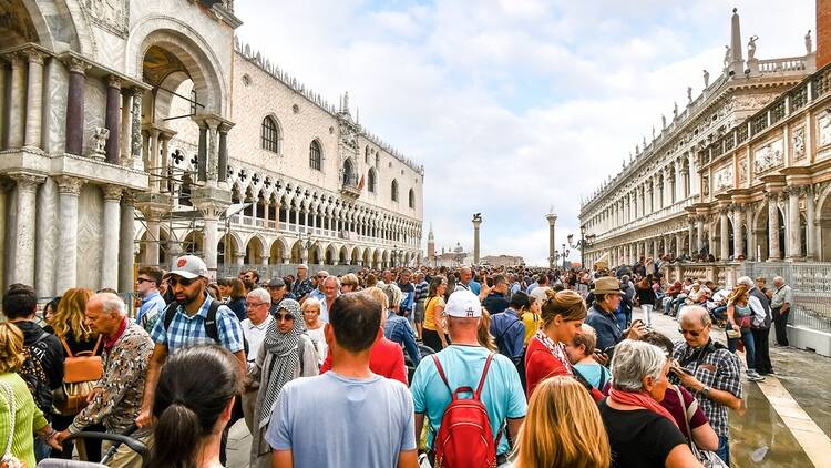 The visible effects of overtourism as cruise ship passengers crowd the walkway at the Doge's Palace in Piazza San Marco on a busy day in Venice, Italy