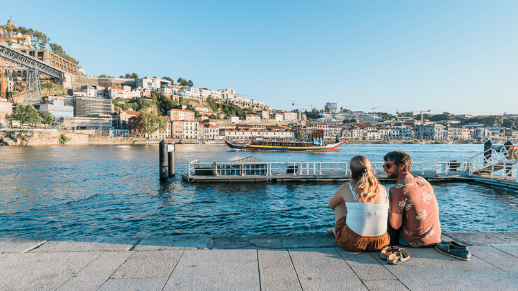 A tourist couple sits in the shore of Douro river, in the famous "Cais da Ribeira" one of the main tourist attractions in Porto. A tourist couple sits in the shore of Douro river, in the famous "Cais da Ribeira" one of the main tourist attractions in Porto.