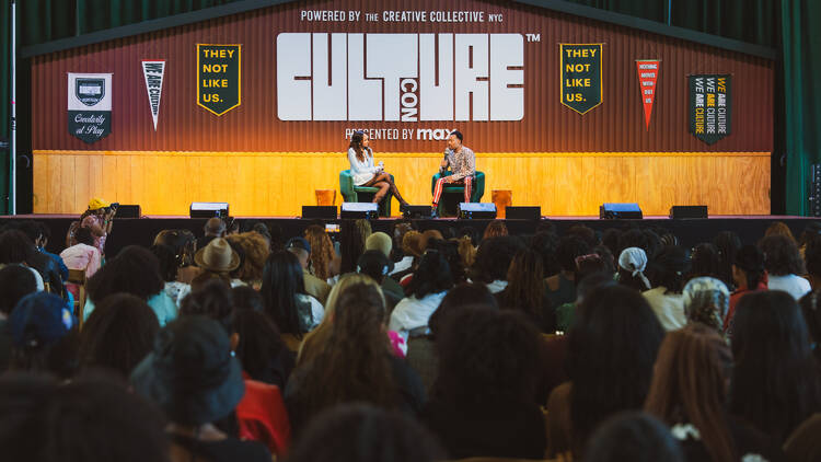 Two people sit on a stage beneath a sign reading CULTURE CON.