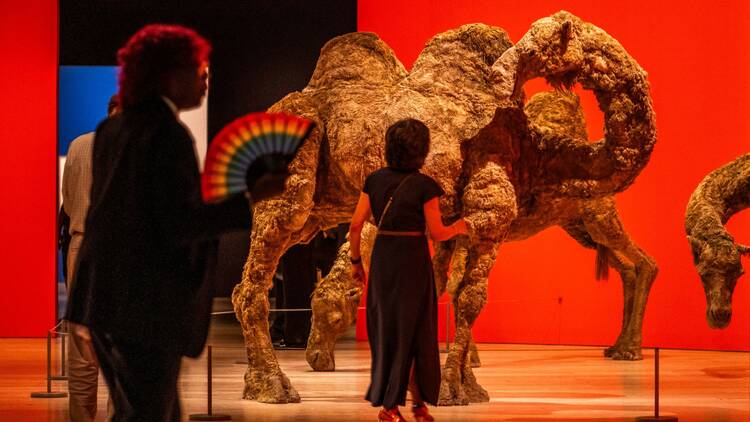 People walk past life-size sculptures of camels.