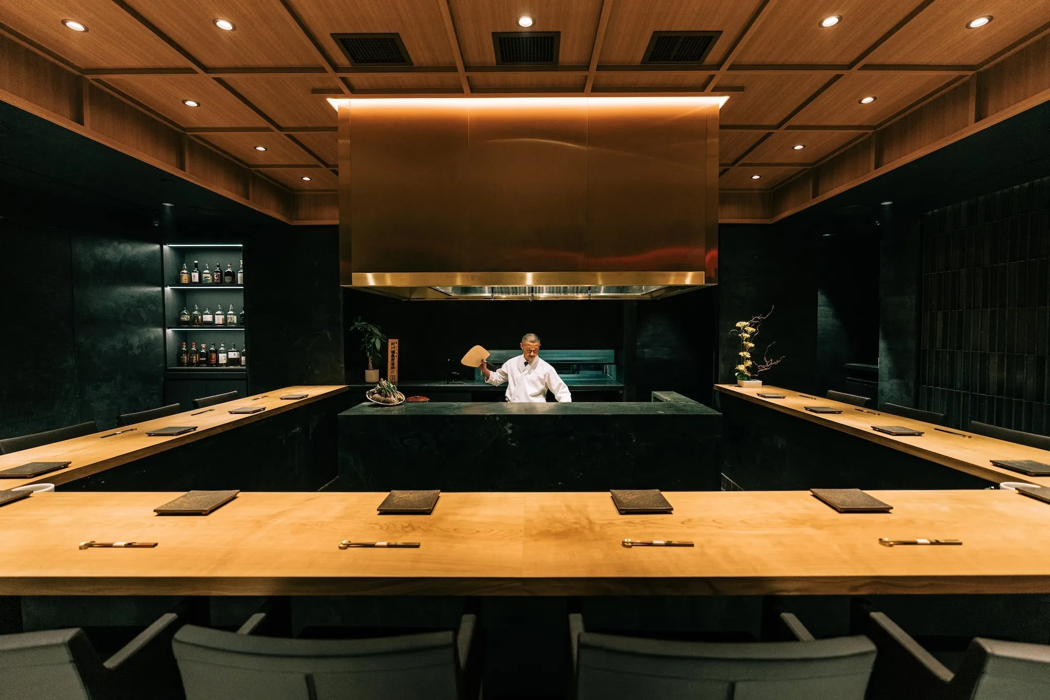 A large wooden table with a chef fanning flames in the kitchen