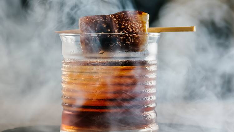 An old fashioned with smoke in the background, garnished with two charred marshmellows