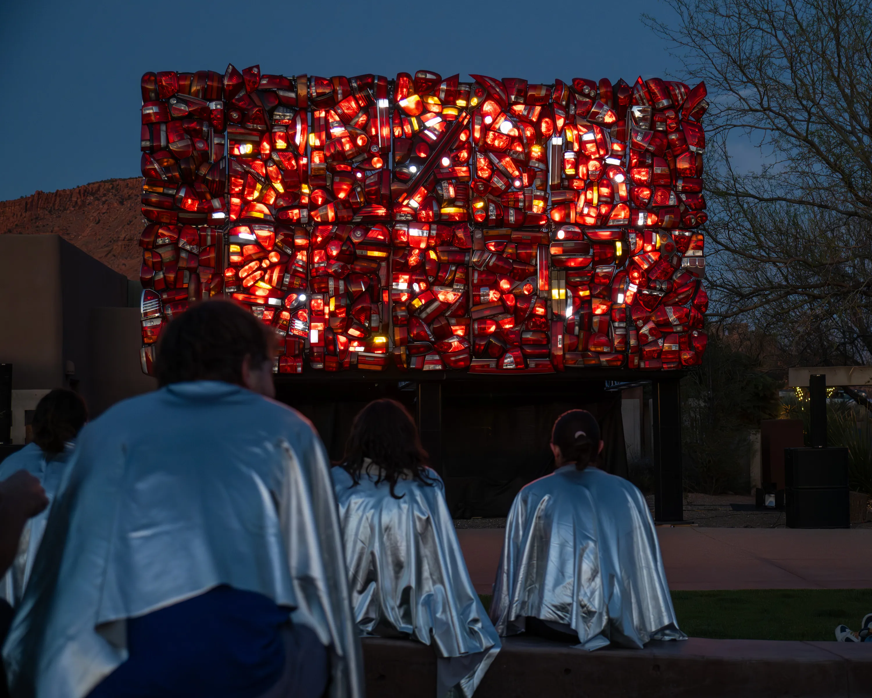 A red wall of lights in front of people wearing silver capes.