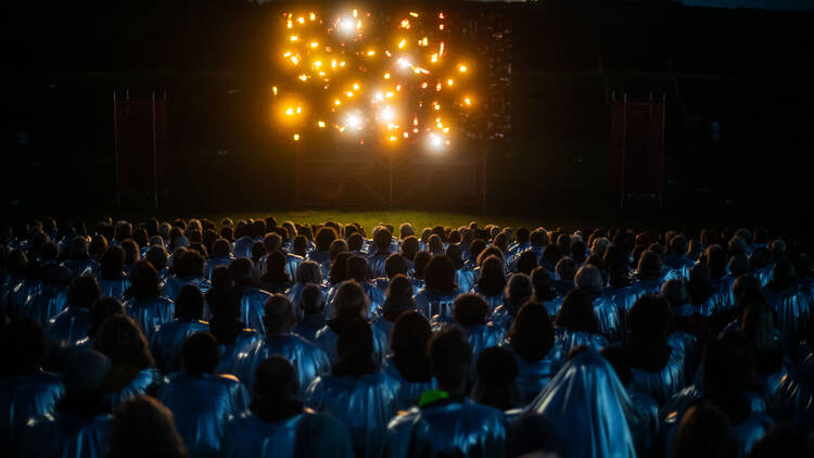 A light show with yellow lights in front of people wearing silver capes.