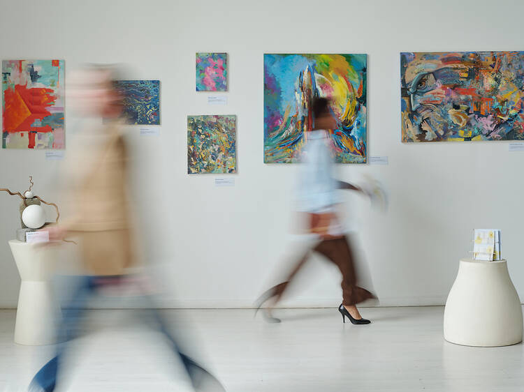 Blurred motion of people passing through the paintings on the wall in art gallery