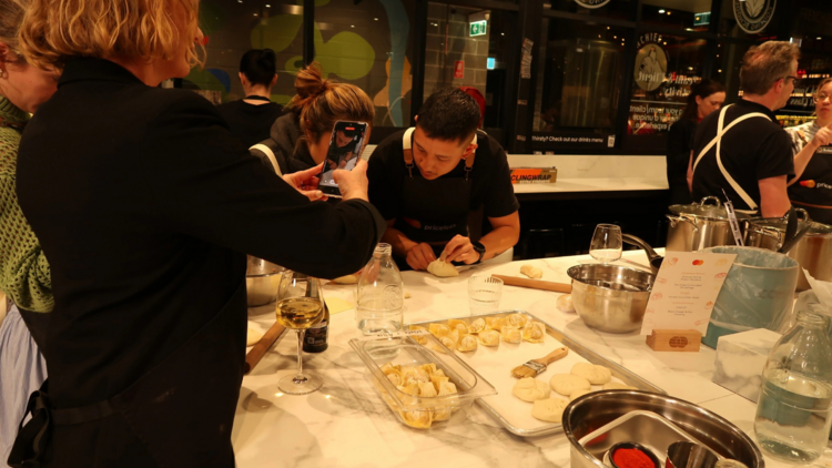 The back of a woman who is taking pics of dumplings and Brendan Pang teaching someone