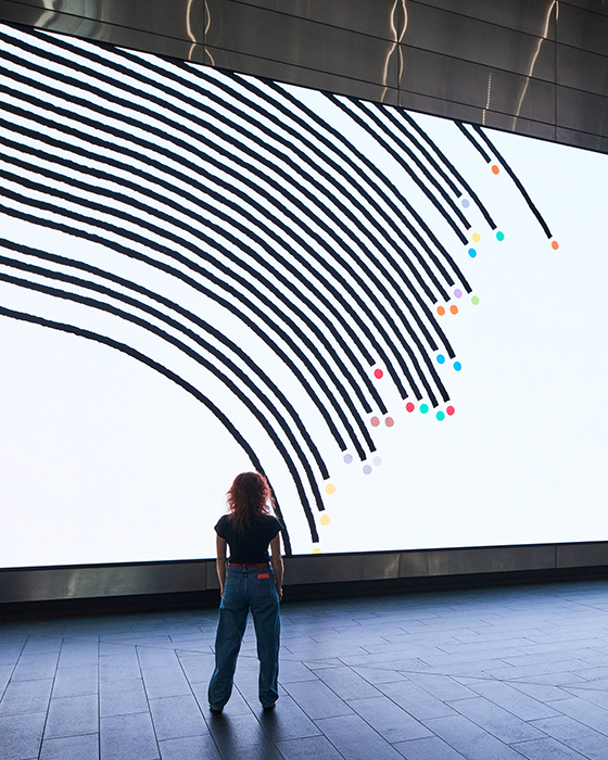 A person stands in front of a black-and-white transit illustration on a digital screen.