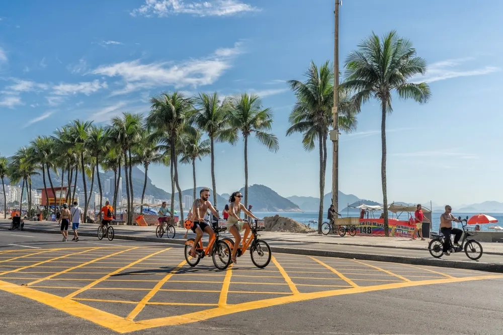 People riding on bikes past Copacabana Beach on a sunny day in RIo de Janeiro, Brazil