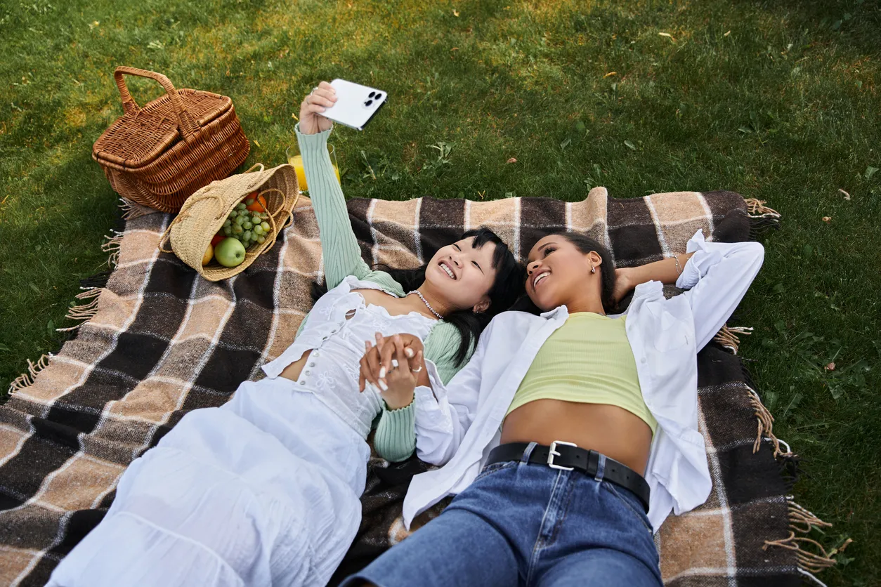 Two diverse women enjoy a joyful moment on a picnic blanket outdoors.