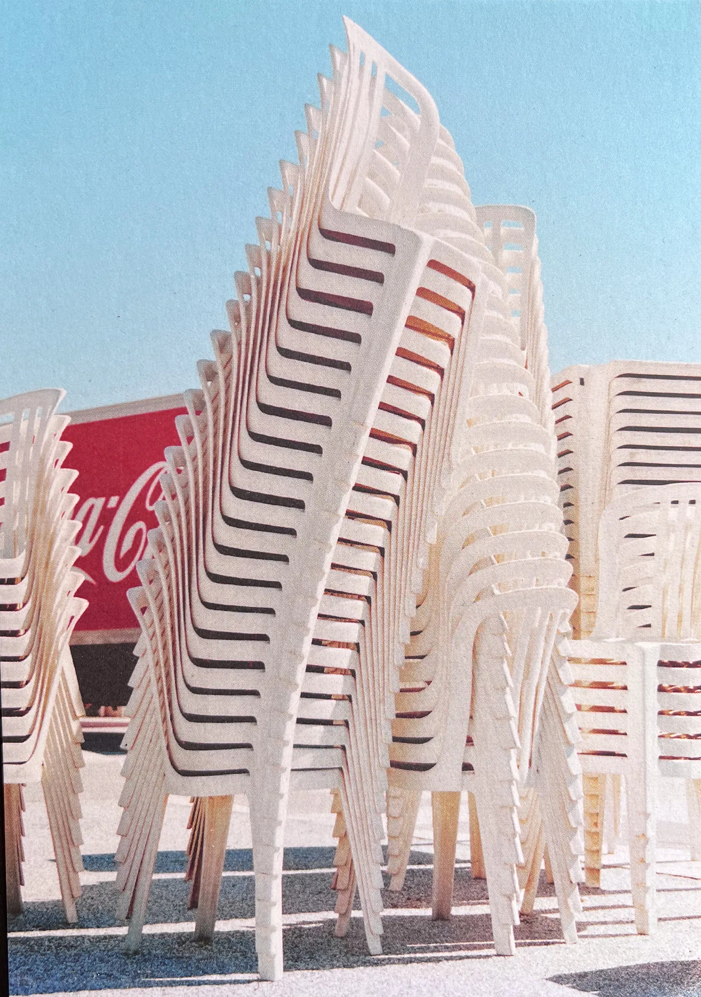 Stacked plastic chairs against a blue sky with Coca Cola truck seen in background