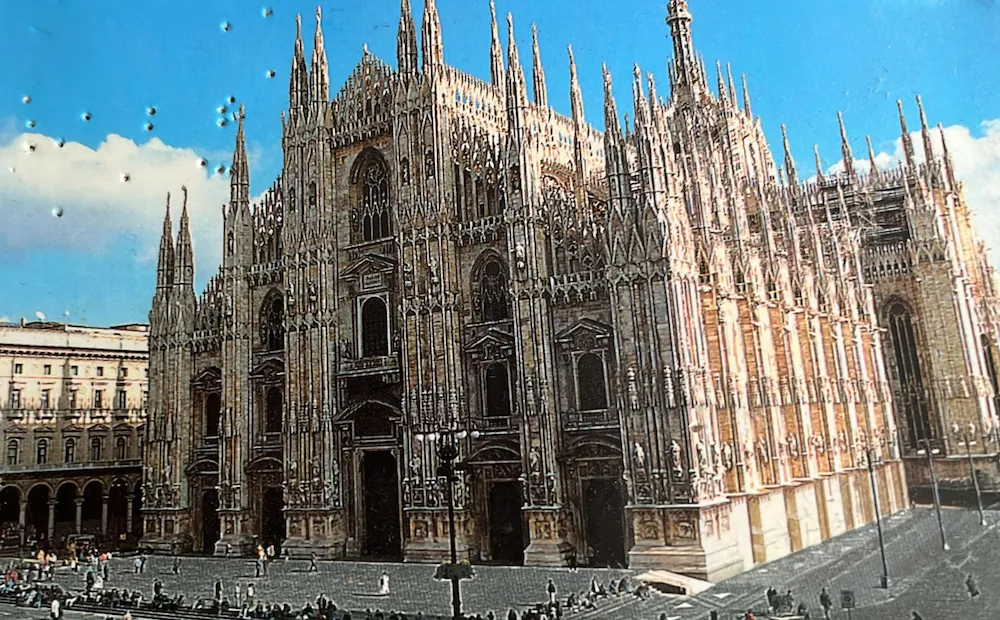 A postcard showing Duomo di Milano, with pinholes from being on a noticeboard