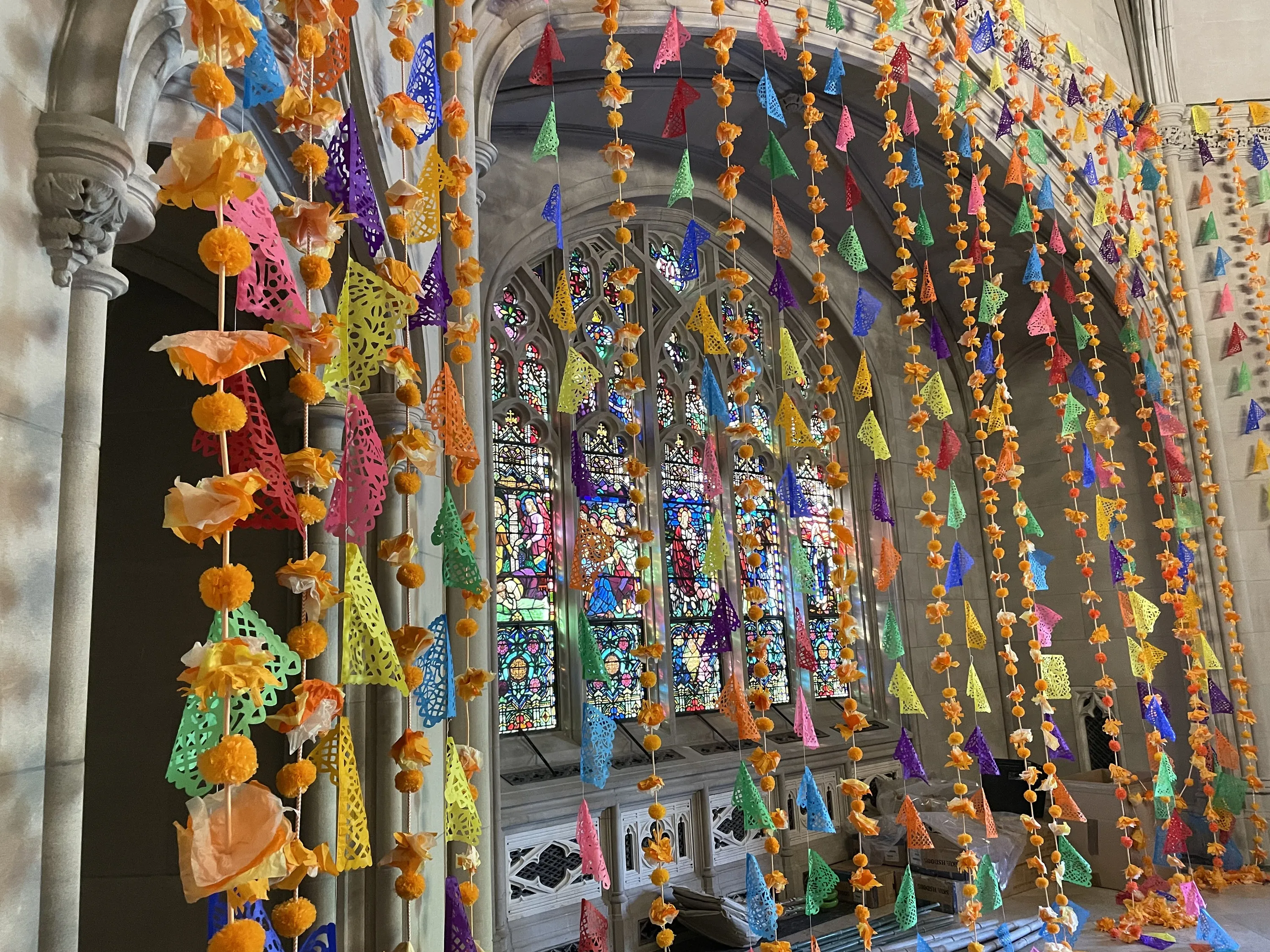 Colorful strands of paper hang down in front of a stained glass window.