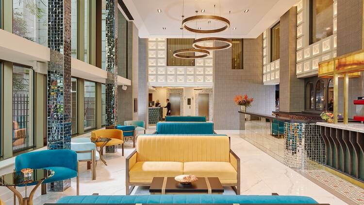 The lobby at the Grafton Hotel in Dublin: high-ceilinged room with polished white floors, blue and yellow sofas, gold accents and pillars decorated like disco balls 