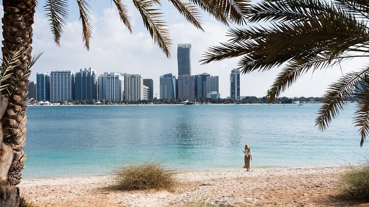 Woman walking on the beach with Abu Dhabi skyline in background