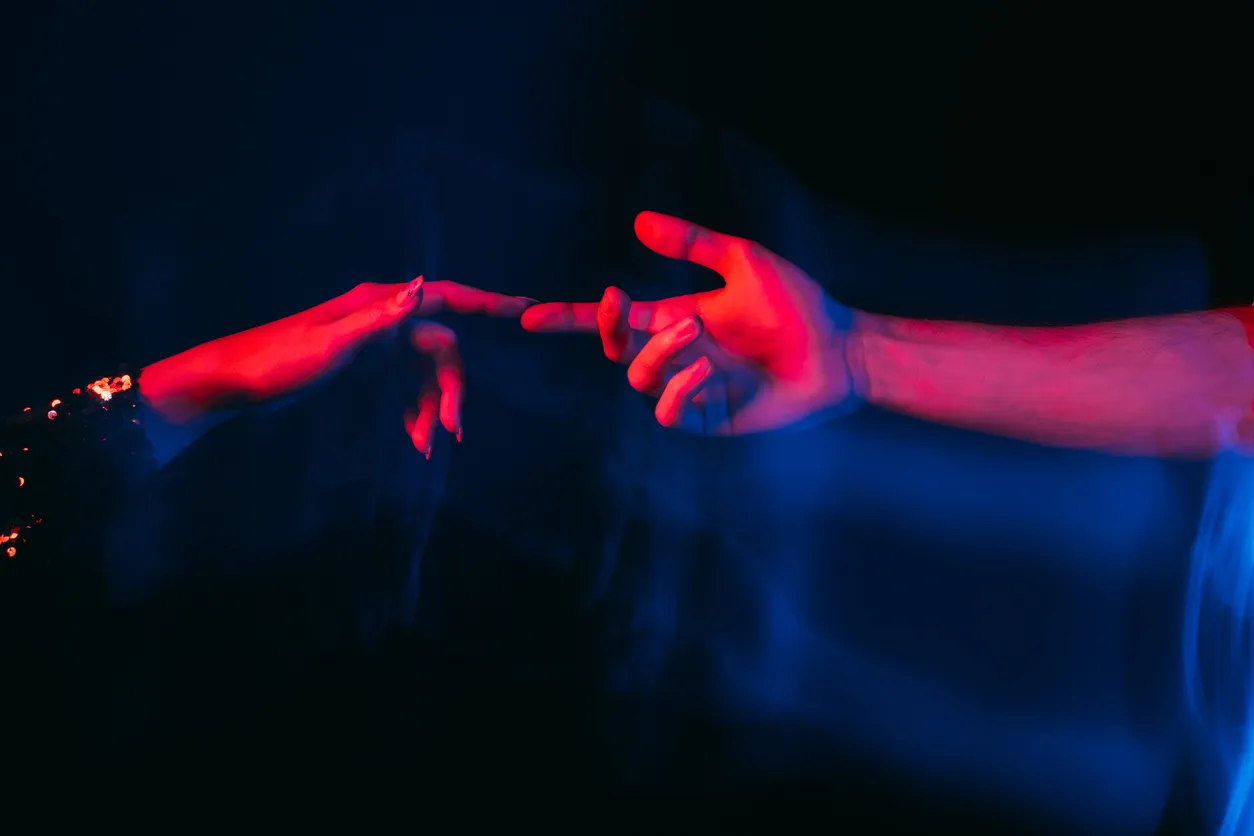 Love power. Romantic couple. Affectionate feelings. Happy meeting. Sensual male and female hands reaching together on blue red neon light blur long exposure isolated black.