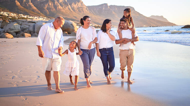 Big family, children or girls bonding on beach on summer sunset holiday, social reunion or vacation. Smile, happy and walking parents, mom and dad with relax senior grandparents and kids in Cape Town