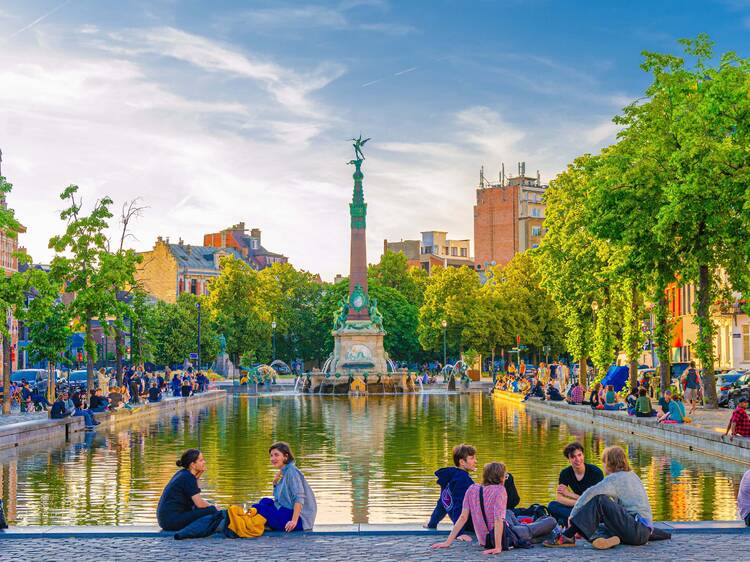 young people tourists sit near small pound with Fontaine Anspach fountain at Old Port Fish market square Vismarkt in old town Brussels city historical center