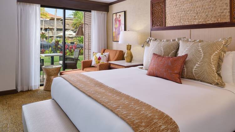 A king bed with orange and yellow accents and views of the green courtyard