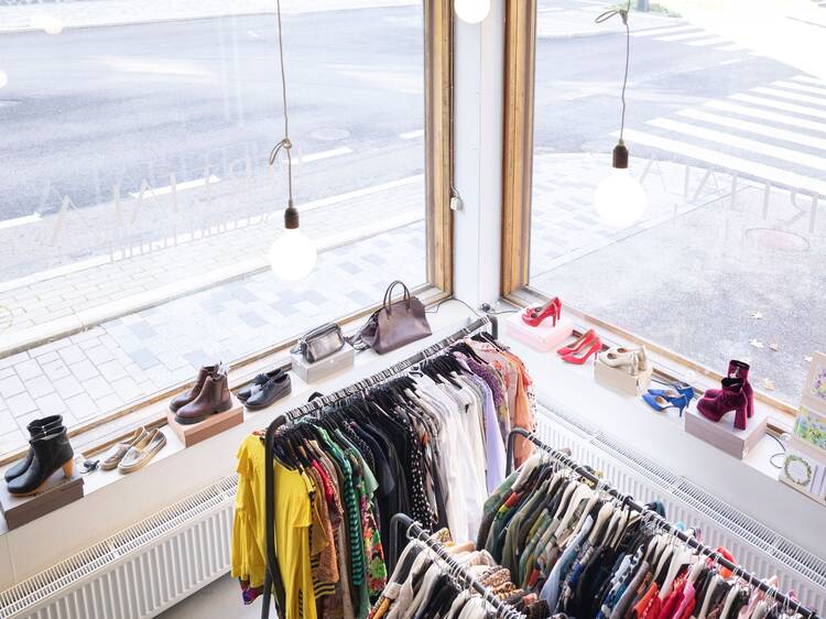 Interior of a second-hand clothing store with racks of colorful garments, a window ledge displaying shoes and handbags, and a view of a pedestrian crossing outside. Interior of a second-hand clothing store with racks of colorful garments, a window ledge displaying shoes and handbags, and a view of a pedestrian crossing outside.