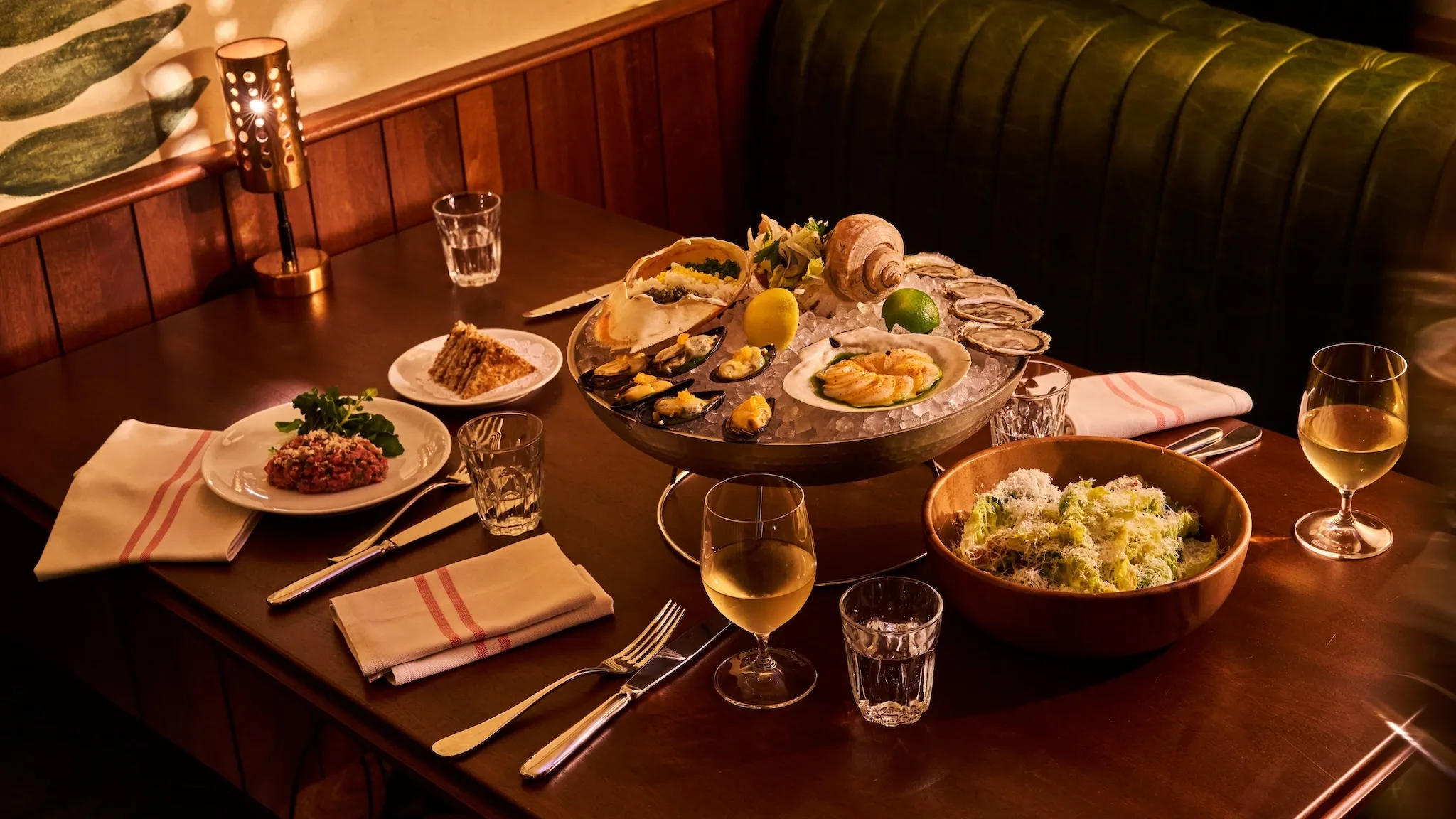 A table with a raw seafood platter, salad, wine and a slice of cake