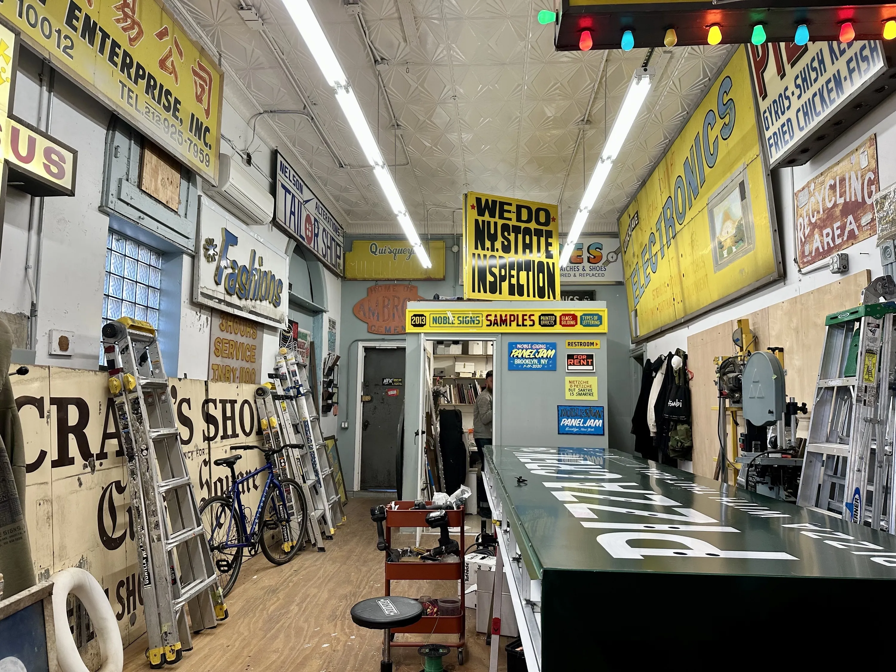 Signs hung up up in a sign museum above a painter at work.