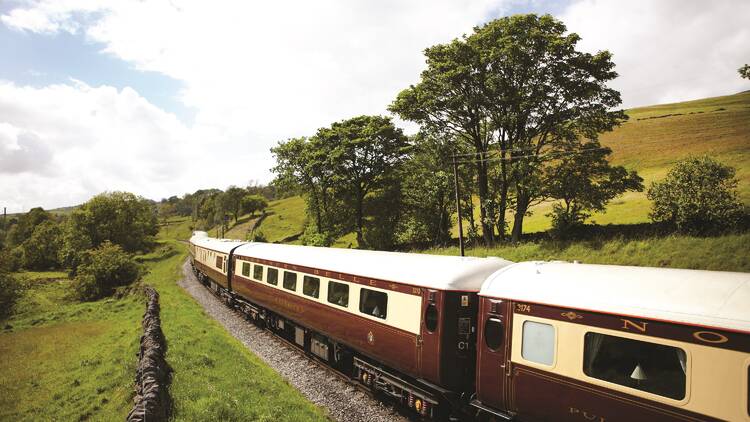 An old-fashioned burgundy and cream train travelling through the British countryside