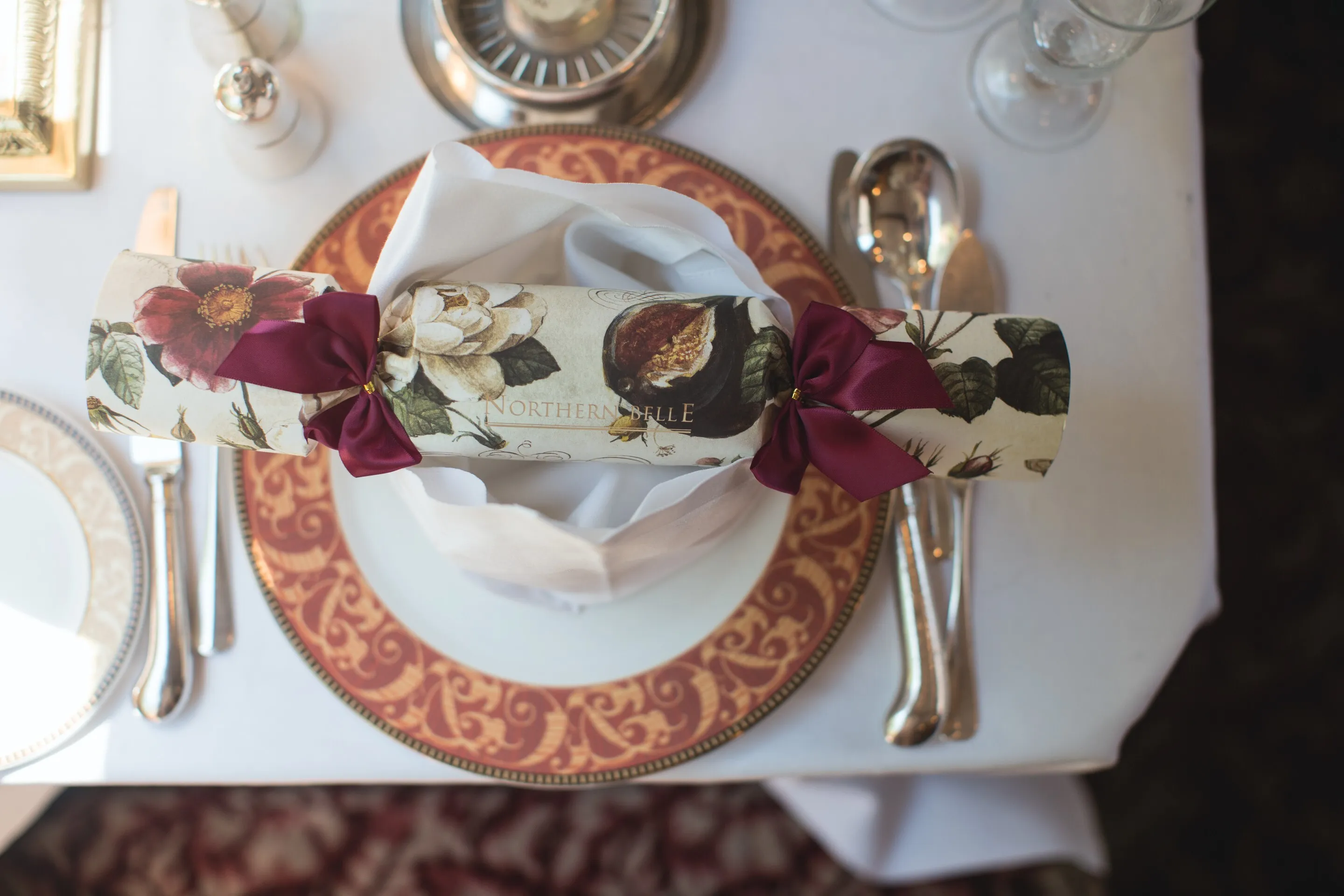 Overhead photo of a table setting on the Northern Belle with silver cutlery, a gold and red plate and a Christmas cracker