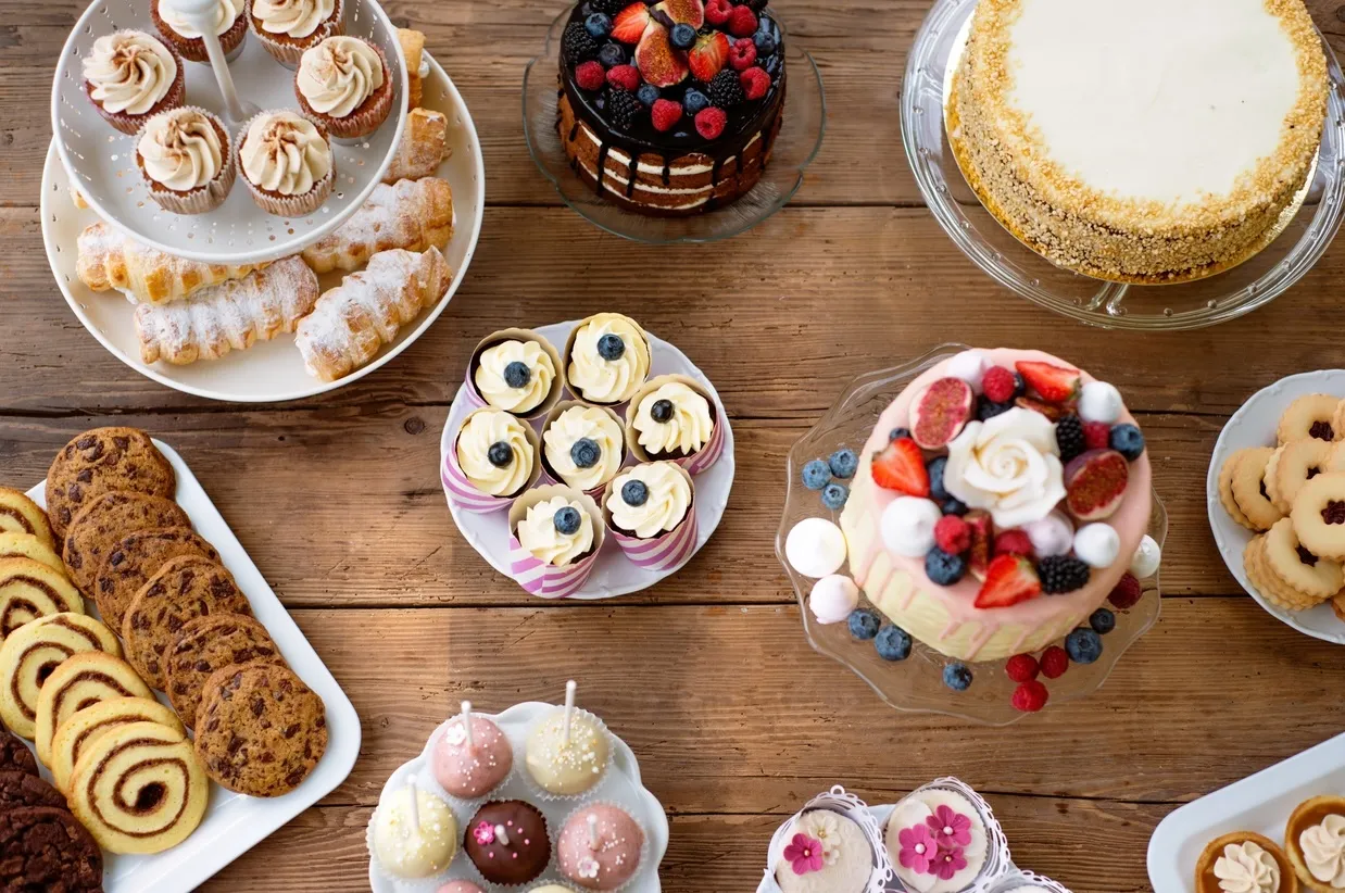Table with cake, pies, cupcakes, tarts and cakepops. Studio shot on brown wooden background. Flat lay.