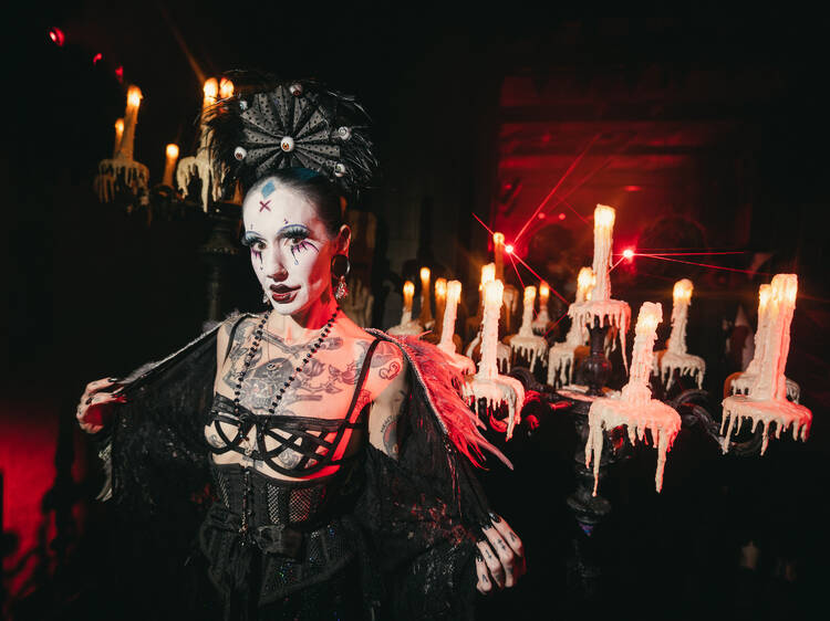 A woman dressed up in a black Halloween costume poses in front of a candleabra.