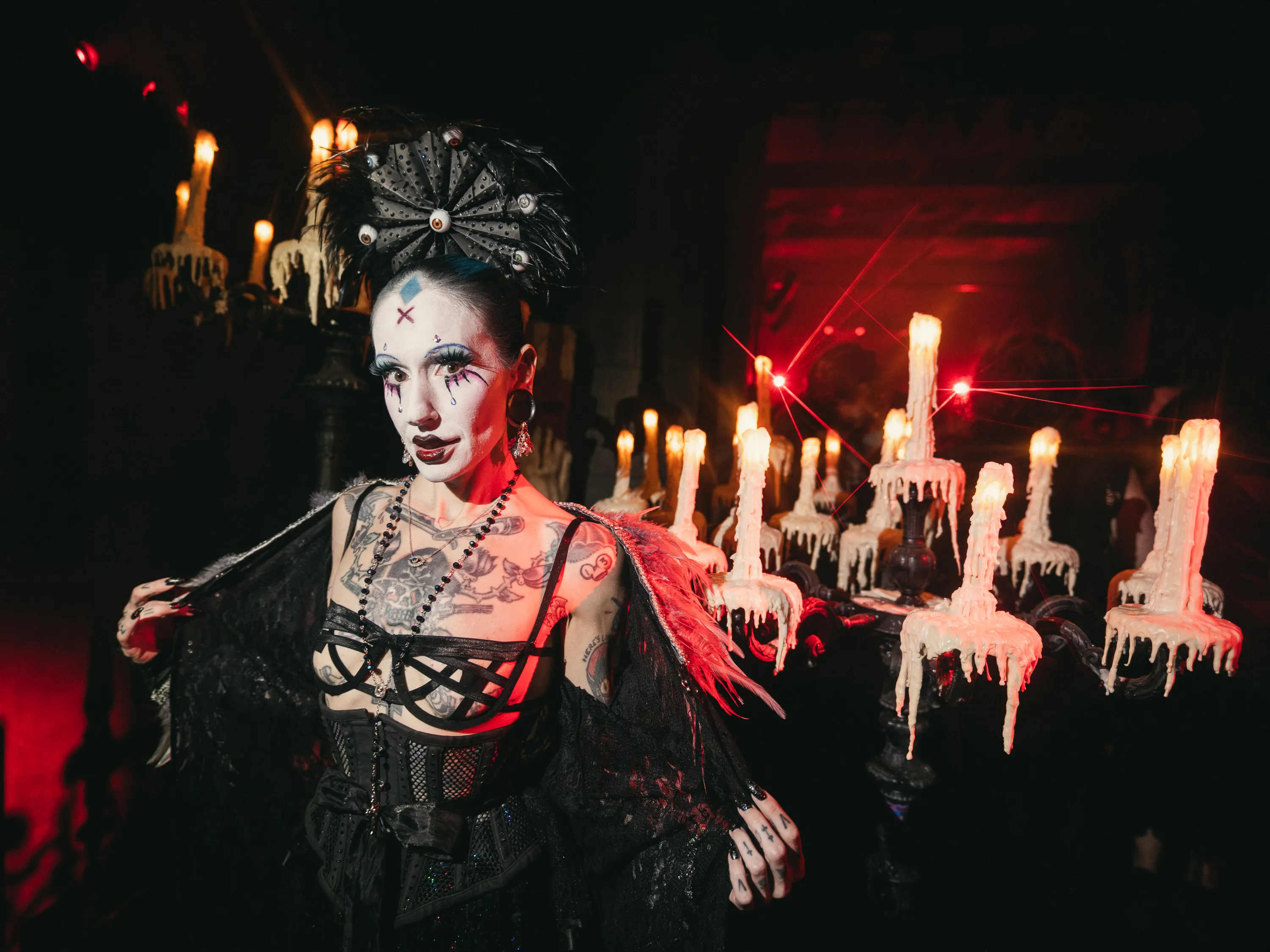 A woman dressed up in a black Halloween costume poses in front of a candleabra.