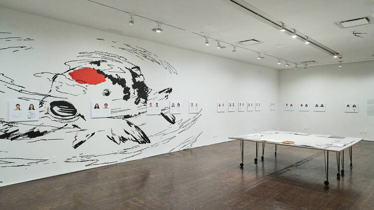 The inside of a photograph exhibit with a mural of a coy fish on the wall and a table in the center with the photos on display