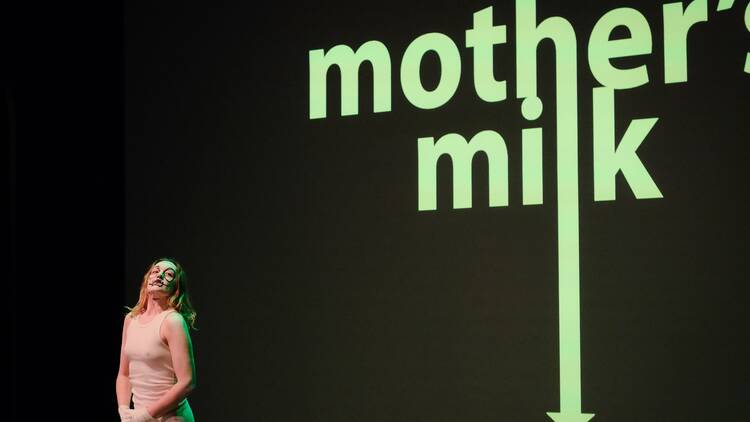 A girl performing on stage in front of a large "mother's milk" logo behind her